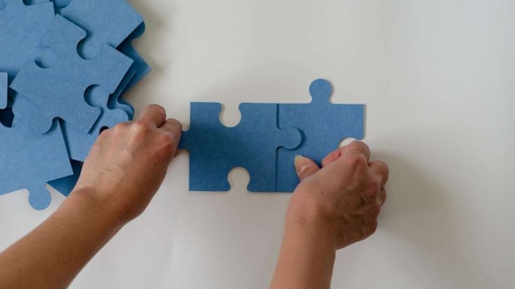 Sieviete salikdama divus puzzle gabaliņus simbolizē, ka kredītu apvienošana ļauj apvienot vairākus maksājumus vienā